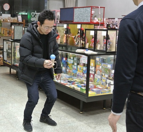 寿月すみたやスタッフS氏のけん玉指導で、10級技の大皿に挑戦中のお父さん。